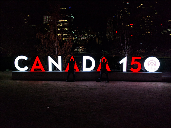 a picture at night of two friends posing as the 'A's' in a Canada 150 sign.