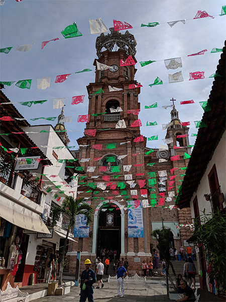 a live look into the streets in Mexico with flags above and a church down the road.